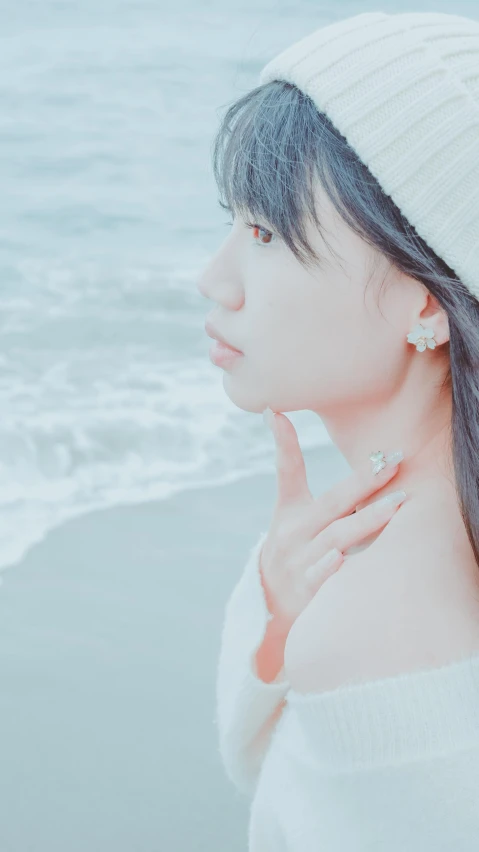 a woman standing next to the ocean with her hand in her ear