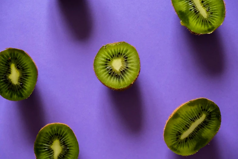 four slices of kiwi sliced on purple surface