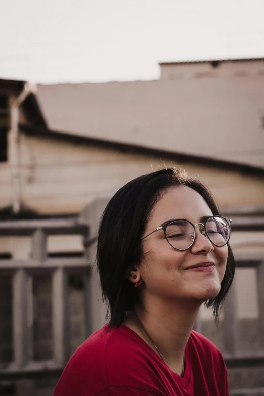 woman in glasses sitting on a deck with a building in the background