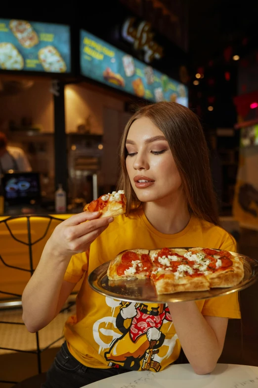 a woman in a yellow shirt eating a slice of pizza