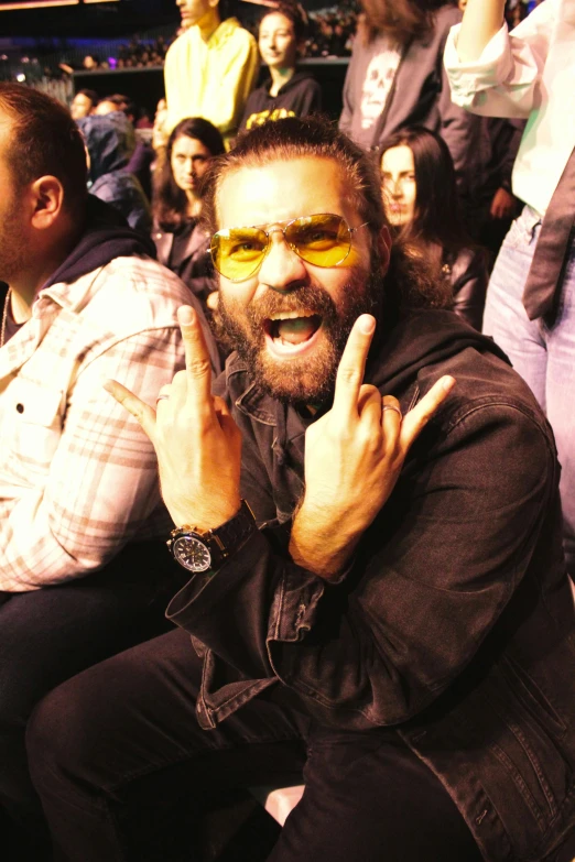 a man in sunglasses smiling as he sits at an event