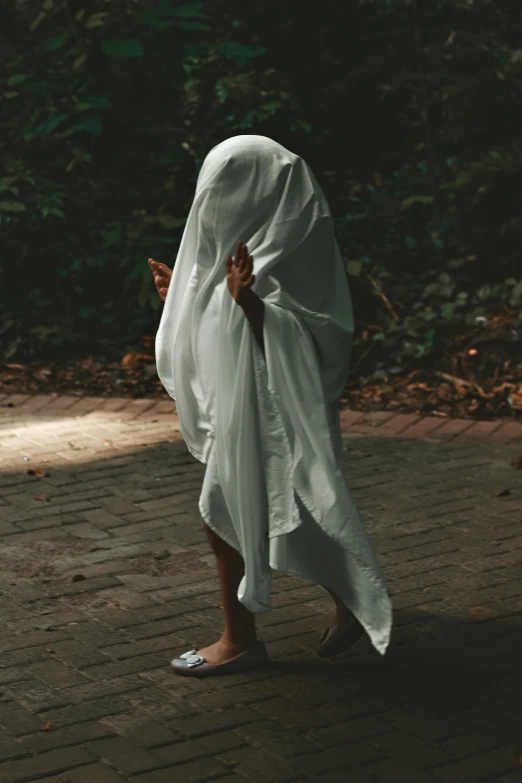 a man covered in a white blanket walking across a sidewalk