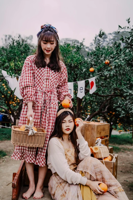 two girls in checkered outfits sitting in an apple orchard with oranges