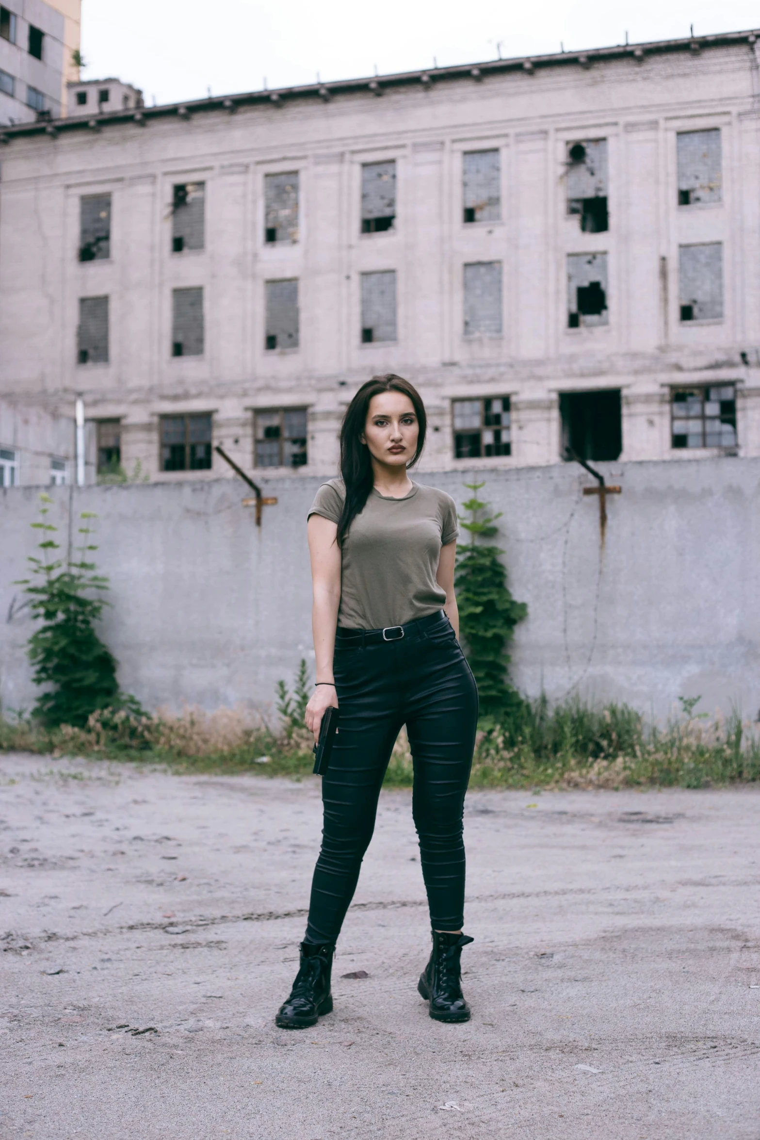 a beautiful young woman standing in front of a rundown building