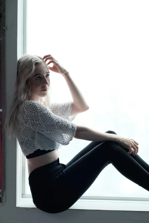 the beautiful blonde woman is sitting on the windowsill