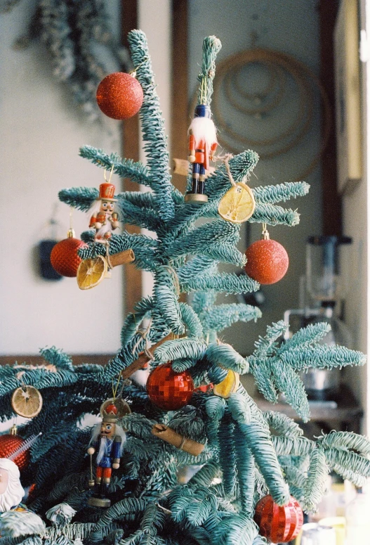 a small christmas tree with orange ornaments and a clock hanging from it's corner