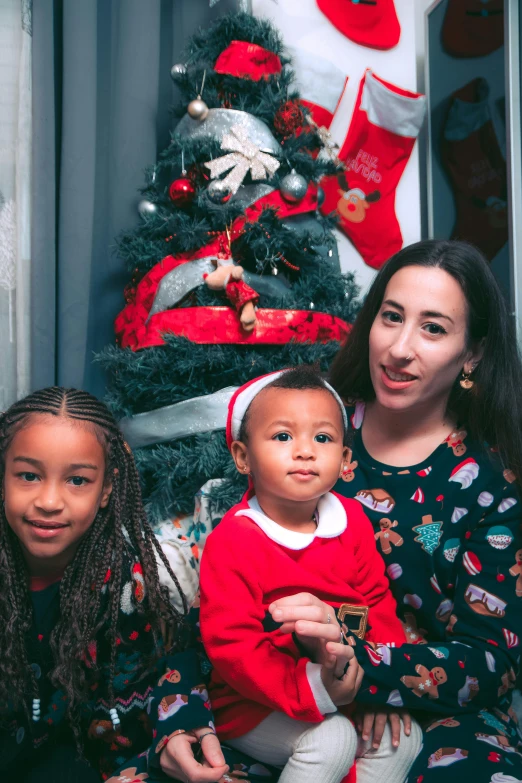 two s and an adult in matching outfits sit by a christmas tree