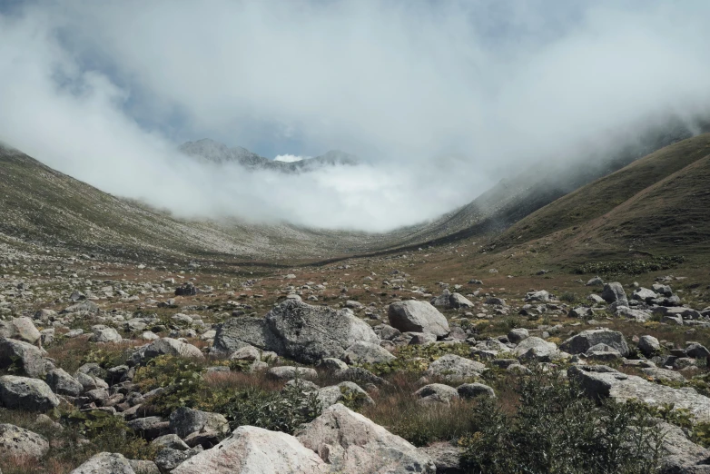 rocks are in the grass as a mountain shroud by clouds