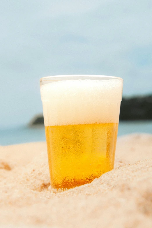 a glass sitting in the sand with water in the background