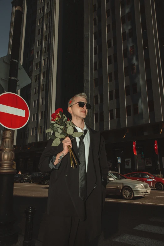 a man in sunglasses is standing outside by a stop sign with flowers