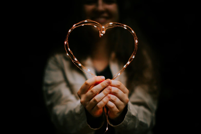 a woman holds out a string heart as she smiles