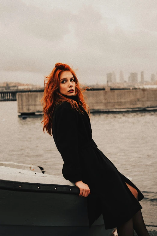 red haired woman posing on a ledge by the water