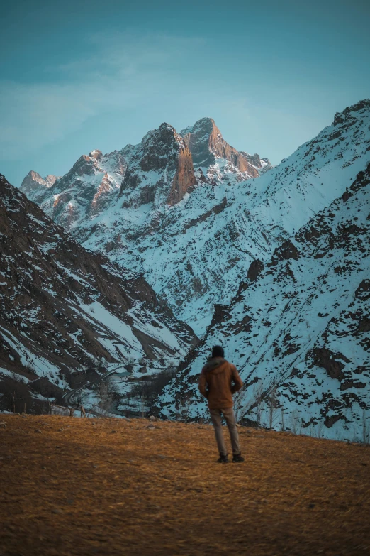 a man walking on a brown field near a snowy mountain