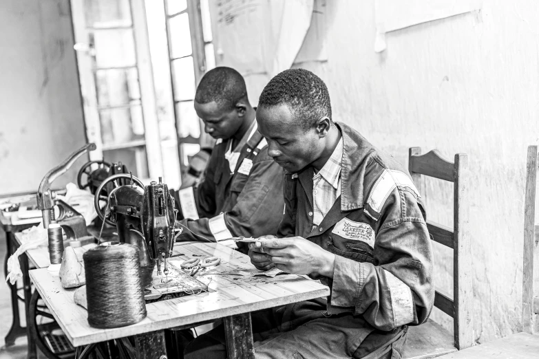 two men sitting at a table with a sewing machine