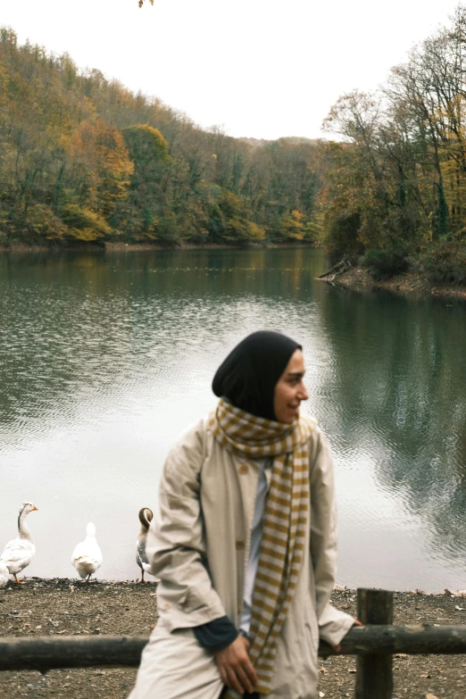 a woman standing near a lake by ducks