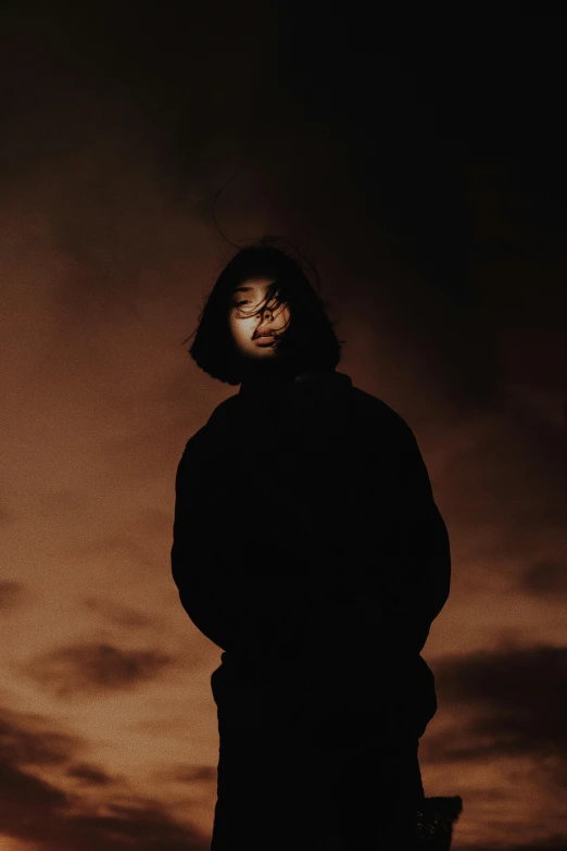 a man in a hoodie standing under a cloudy sky