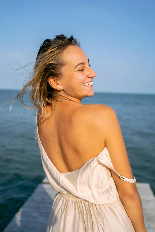 a smiling woman in a white dress is sitting on a dock