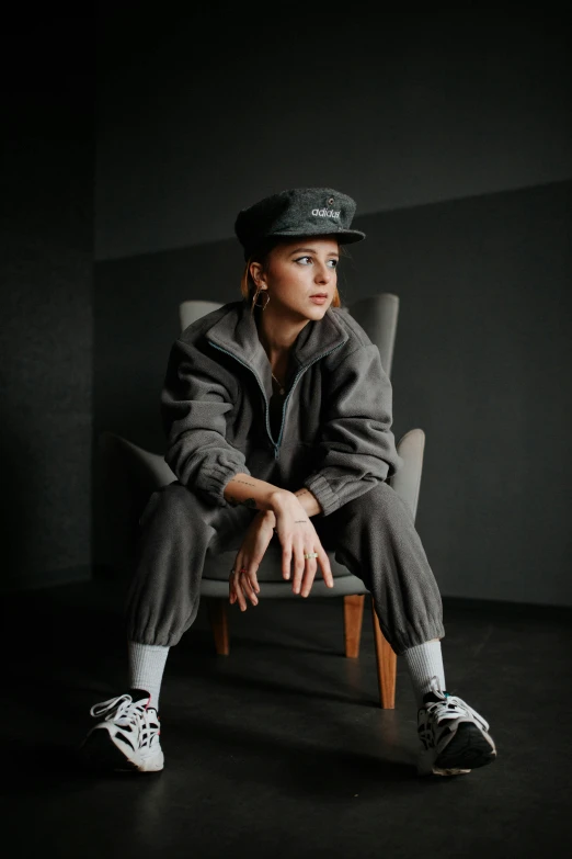 a woman is sitting on a chair wearing a gray jacket and hat