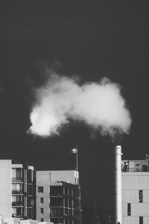 smoke billows from stacks of building behind a flagpole