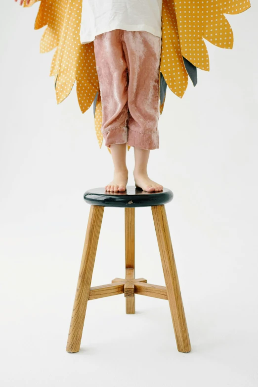 the little girl is standing on the stool holding a large doll's wings