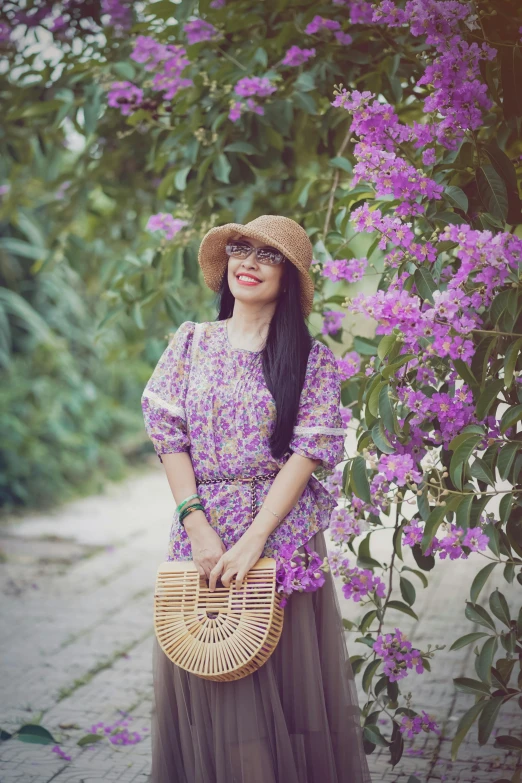 woman in hat, dress and long skirt in front of flowers