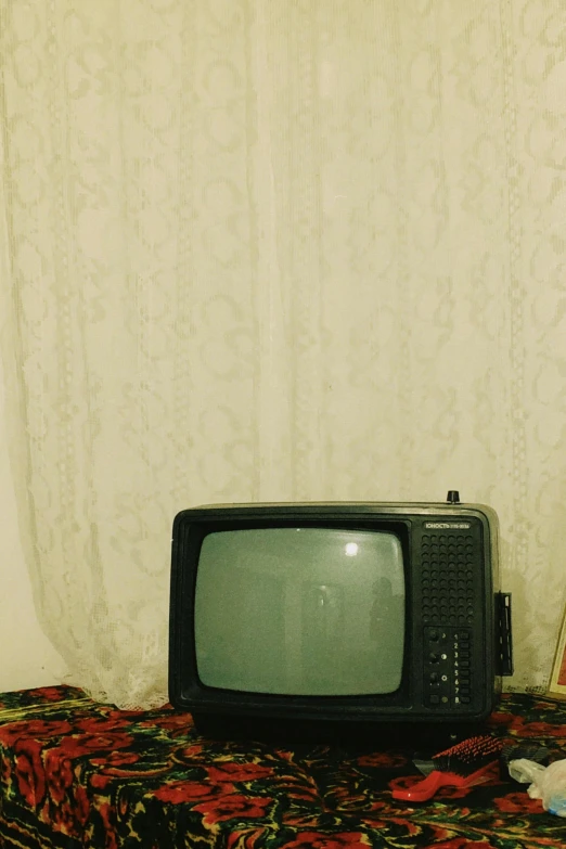 an old tv sits on the ground in front of a curtain