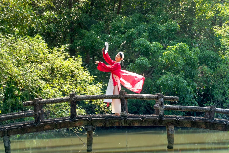 an asian woman is dancing on a wooden bridge over the water