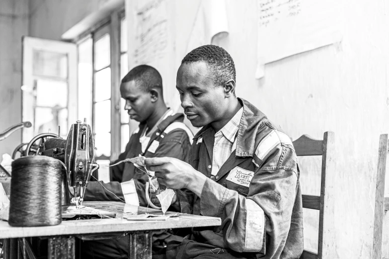 men sitting at a table in front of sewing machines