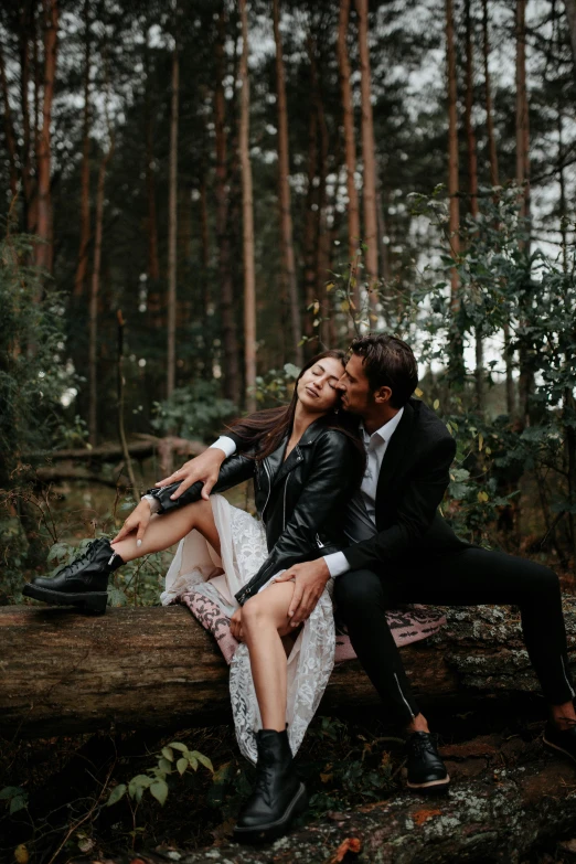 a man and a woman kissing on the end of a log in a forest