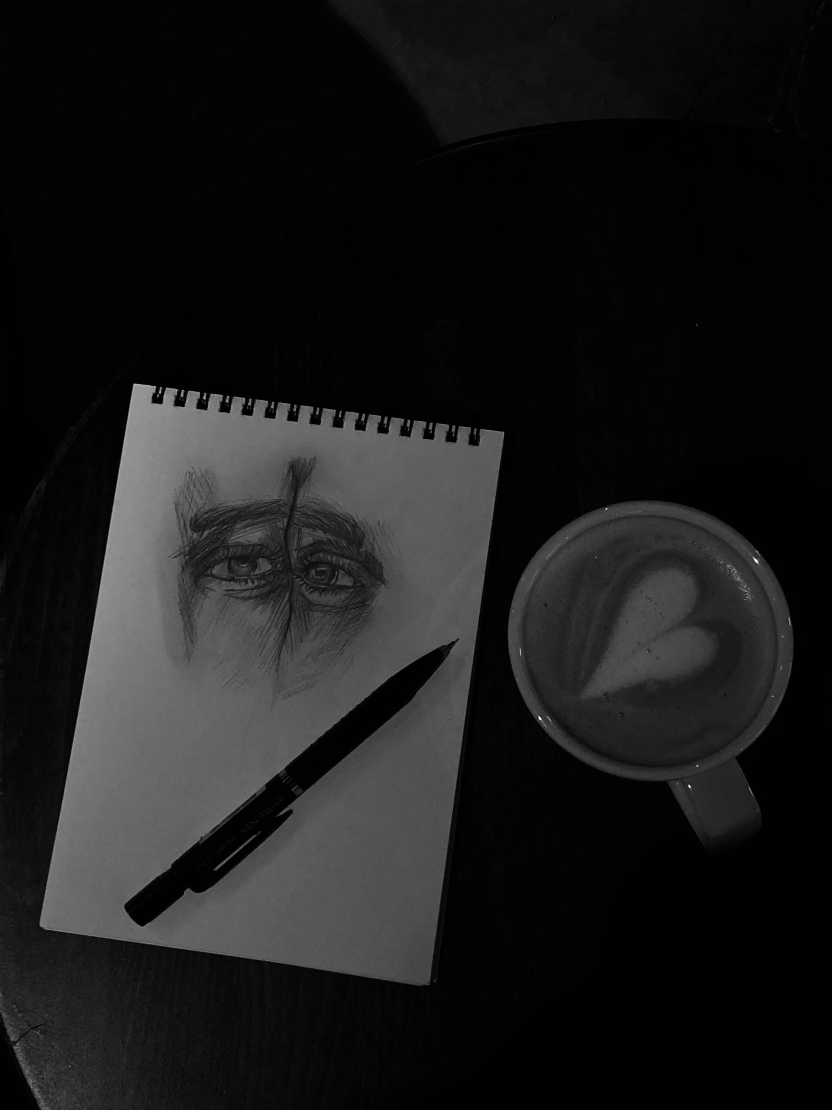 the eye is drawn on paper beside a pencil, cup, and a pen