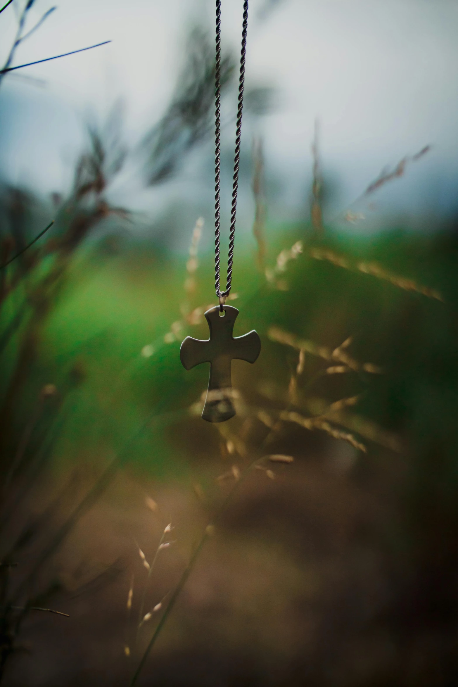 a small wooden cross necklace hangs from a chain in a grassy field