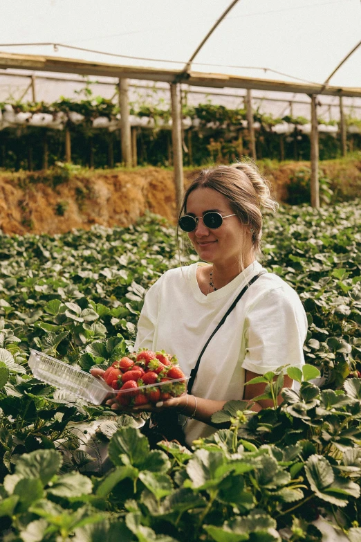 a woman holding a bouquet of flowers standing in the middle of a greenhouse