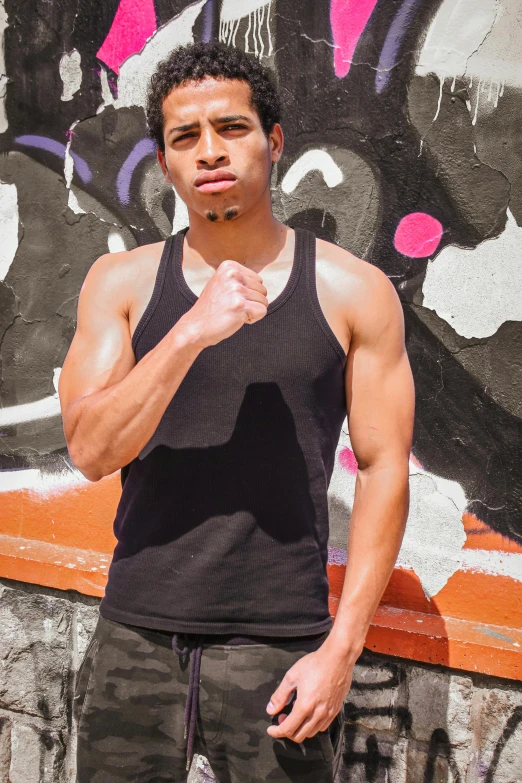 a man standing against a graffiti wall with his hand under his chin