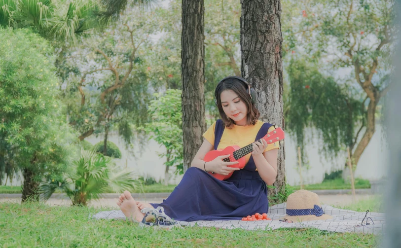 a woman sitting in the shade holding an orange guitar