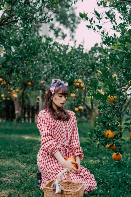 a woman sitting down in the grass holding a basket