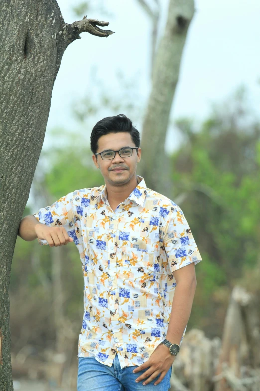 a man in a floral shirt standing by a tree