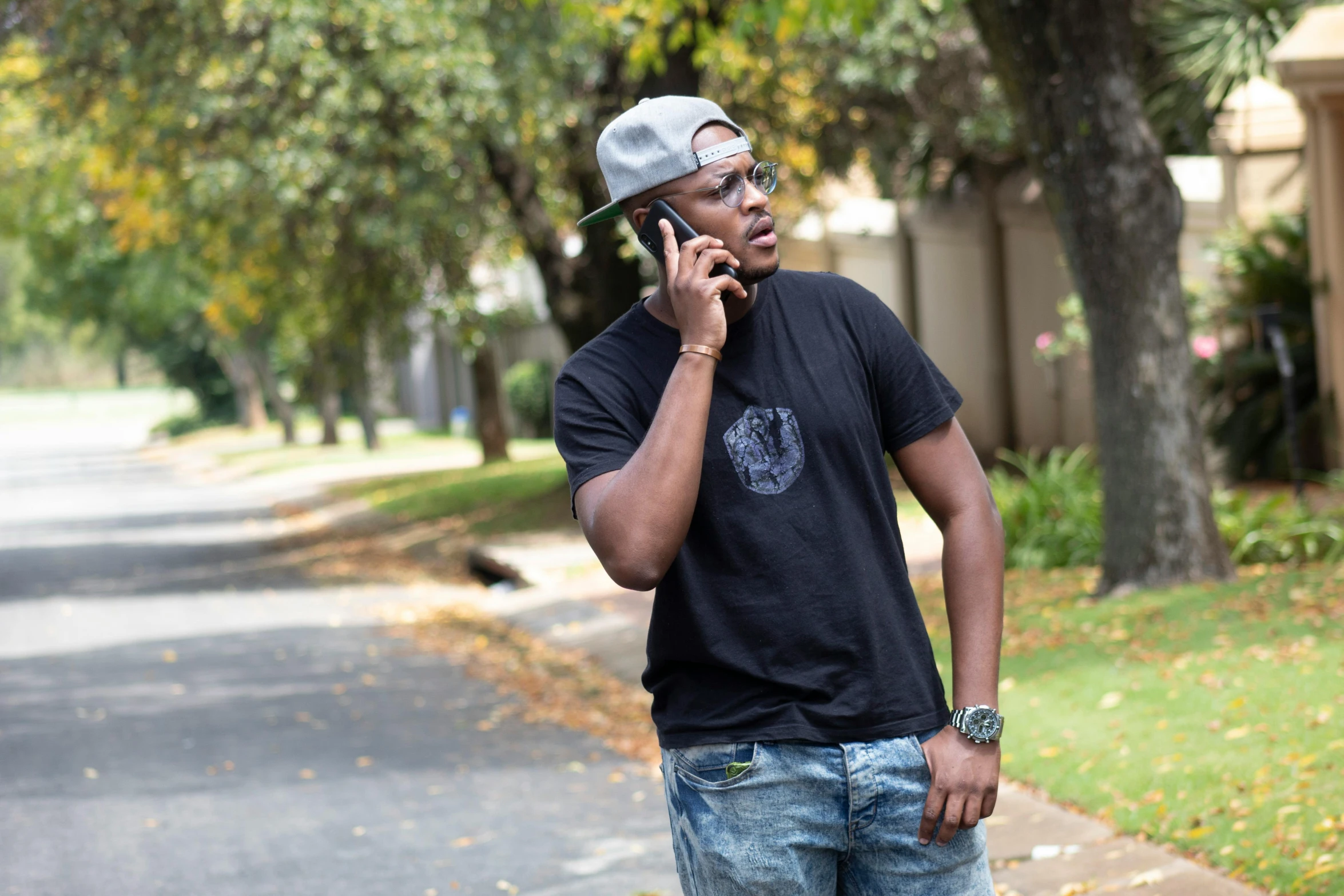 a young man standing on the sidewalk holding his cell phone to his ear