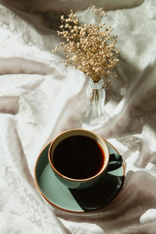 a cup of coffee and vase with baby's breath sitting on a table cloth