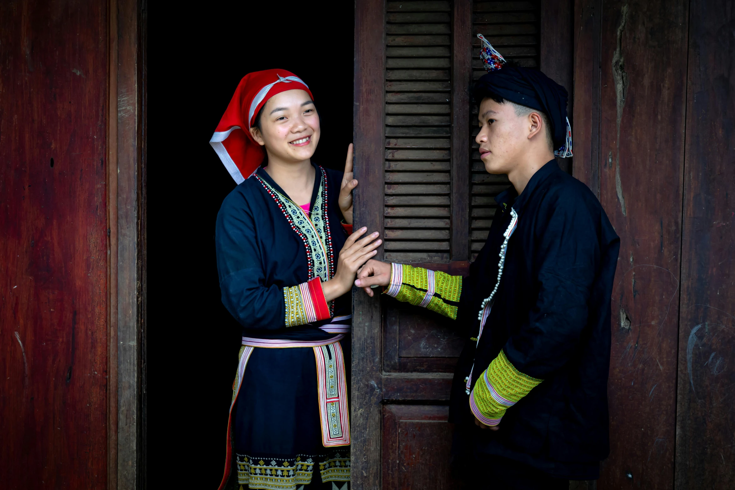 two young people dressed in traditional clothing and turbans stand beside the door