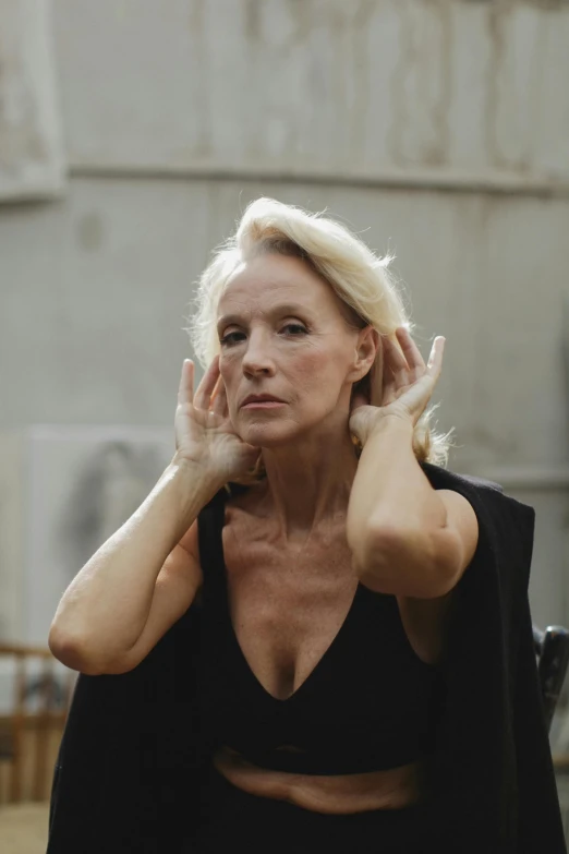 a woman poses wearing a black outfit with her hands on her head