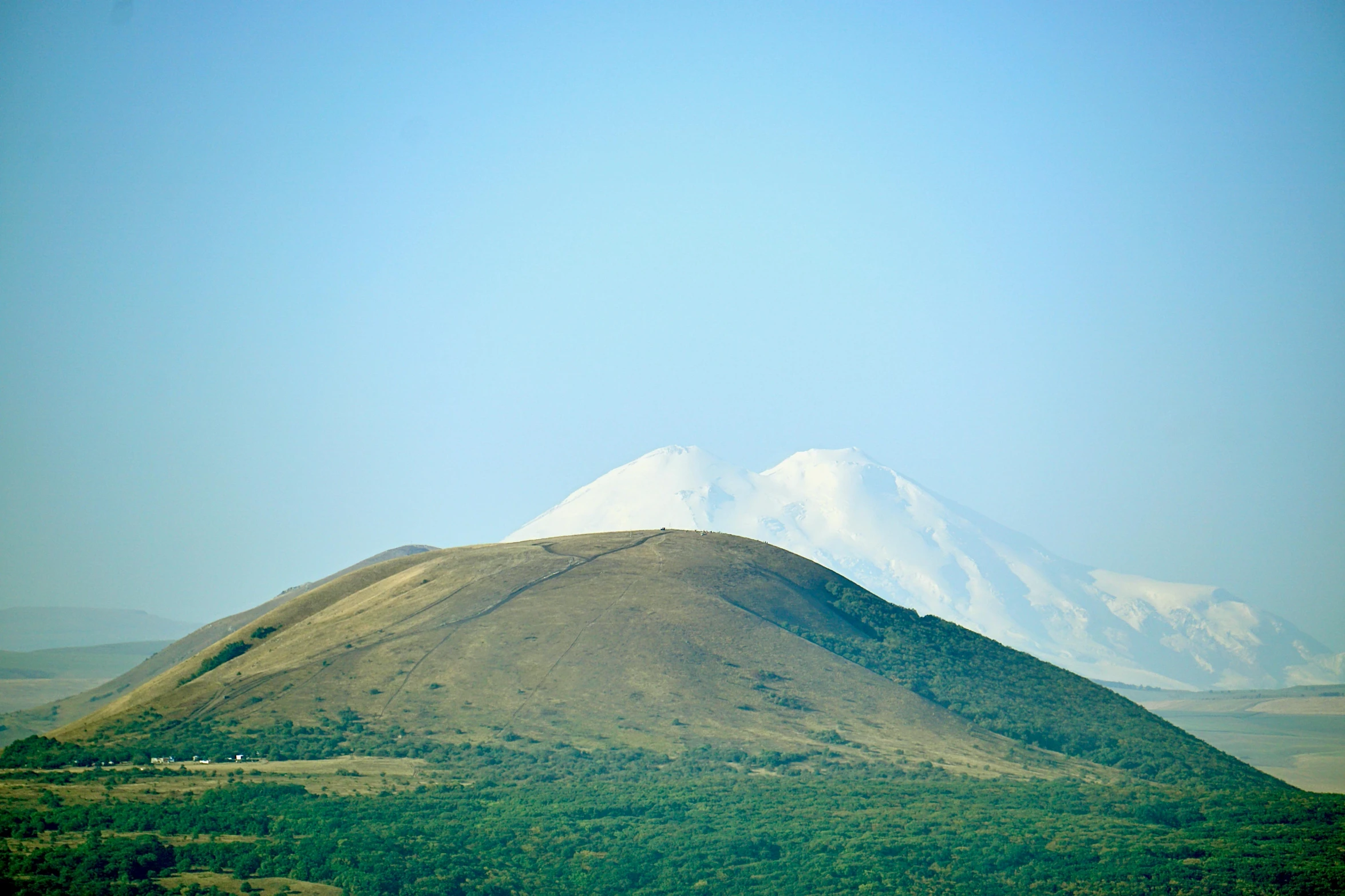 a hill that is covered in grass near some mountains