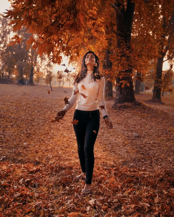 a woman holding two cat paws while walking through autumn leaves