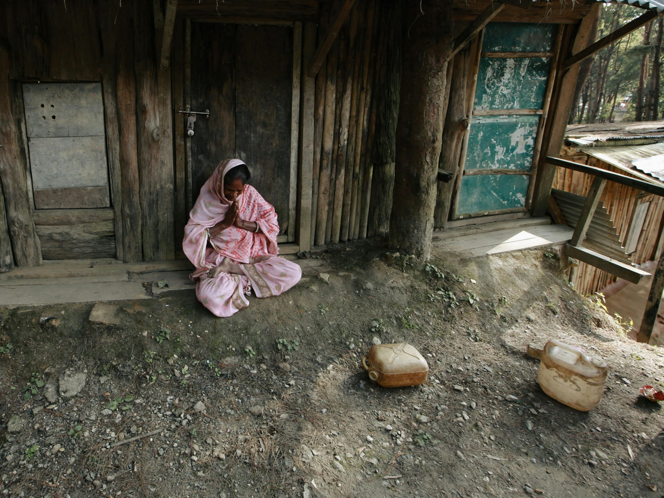 an old woman sitting in front of her shack with bags