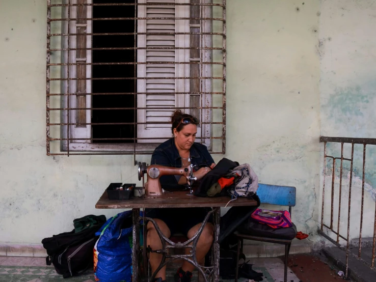 a person sitting on a table with luggage and an iron grilled window in the background