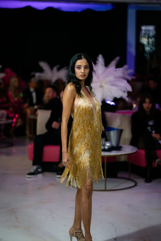 a woman wearing a gold dress at a fashion show