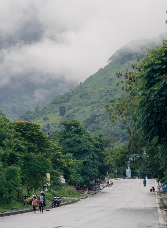 people walk down an empty road with mountains in the background