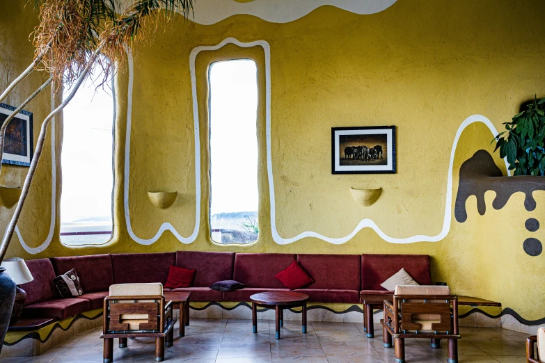 a living room with a yellow wall, a bench and wooden chairs