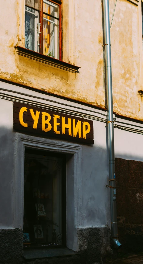 a small shopfront with bright yellow letters is next to an old building