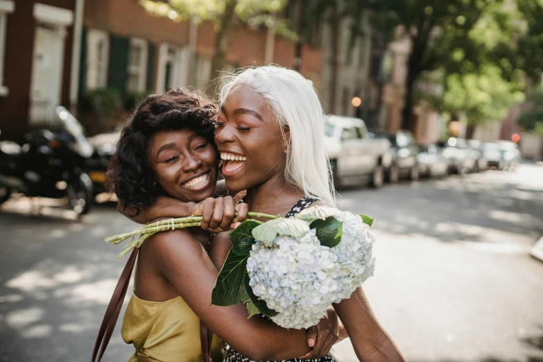 two women with white hair are hugging on the sidewalk