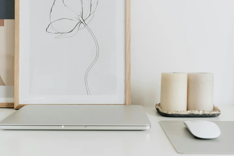 a white laptop computer sitting next to a painting and two candles